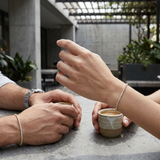 Wide shot of male and female hands with slim yellow gold lab-grown diamond bracelets in a stylish outdoor urban setting, showcasing elegance and modern design.