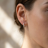 Full-body view of a female model wearing elegant white gold diamond huggie earrings, showcasing their subtle sparkle and lightweight design in a modern setting.