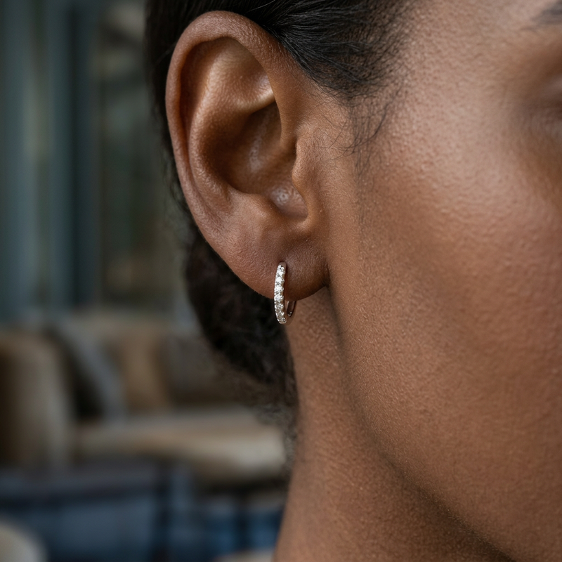 Macro shot of Elina 14K white gold diamond huggie earrings on a dark female ear, highlighting craftsmanship and sparkling diamonds.