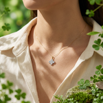 Wrist shot of the Alina Clover Pendant necklace in a lush garden setting, emphasizing delicate design, fine chain, and natural size with soft lighting.