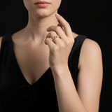 A studio scene with a female model standing against a sleek, dark velvet backdrop, illuminated by an HDR studio light that enhances the sparkle of the diamond ring. She wears a fitted, elegant evening dress with bare shoulders, and her arm is raised, showc