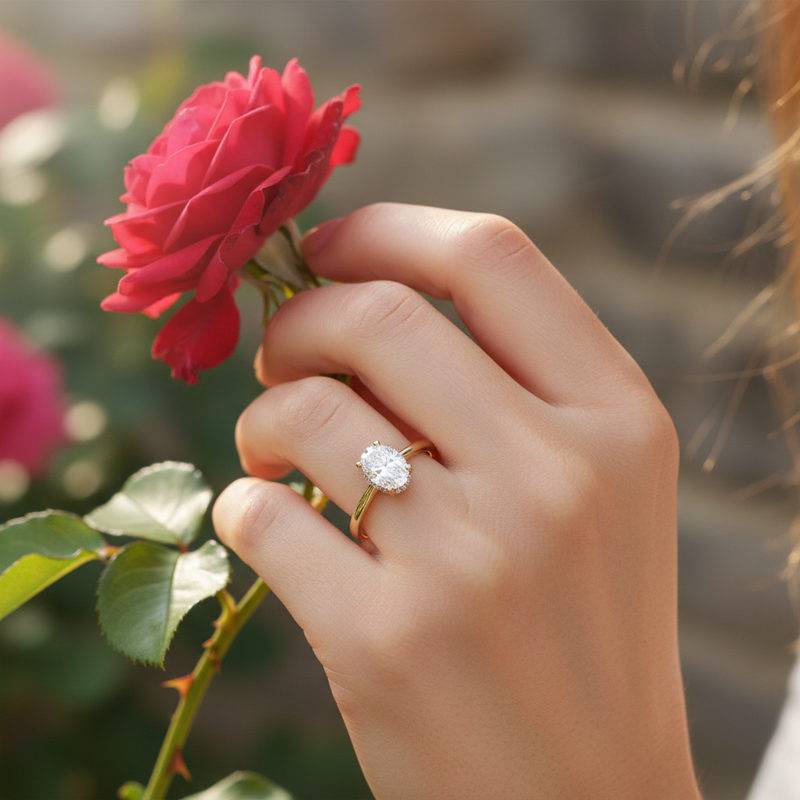 Lifestyle shot of female hand with Hera ring in romantic setting, emphasizing the oval cut diamond detail.