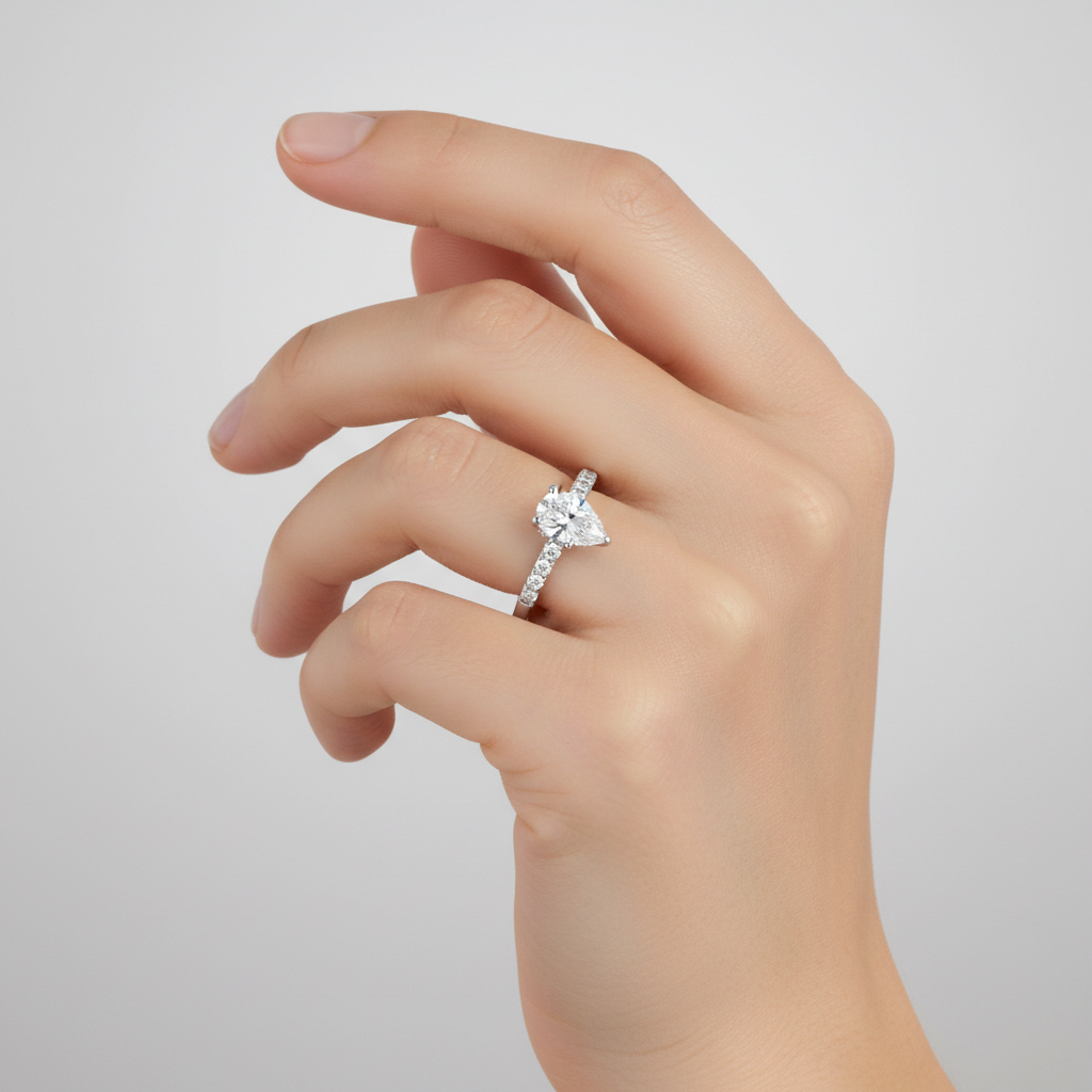 Capture a close-up, studio-quality image of a female hand elegantly wearing the Rasha 14K White Gold Pear Lab Grown Diamond Hidden Halo Engagement Ring. Use diffused daylight studio lighting with a subtle rim light to highlight the pear-shaped solitaire di