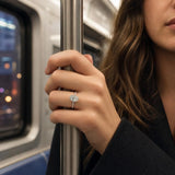 Close-up of Adriana engagement ring on hand with city lights in background, showcasing the oval lab-grown diamond and hidden halo.