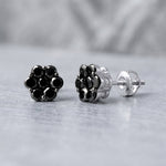 Close-up of 1.1ct black diamond cluster studs in 10K white gold, highlighting their intricate design and sparkling diamonds with soft natural lighting.