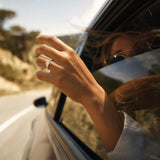 Cushion cut lab grown diamond engagement ring set in 14K yellow gold, worn on fingers outside a moving vehicle window during a summer road trip.