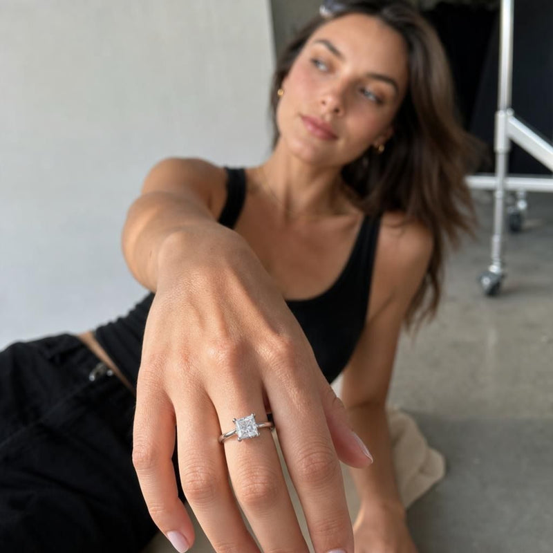 Model wearing Genoveva 14K white gold princess cut lab-grown diamond engagement ring with hidden halo, in a candid studio scene.