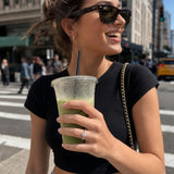 Model carrying oversized iced matcha with ring wrapped around cup, showcasing engagement ring in candid street-style shot.