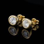 A close-up studio shot of the Alisha 1.5 Ct TW Non Certified Lab Grown Round Diamond Studs Bezel 14K Yellow Gold Earrings, photographed with a softbox lighting setup that highlights the brilliance of the diamonds and the warm tone of the gold. The camera i