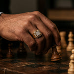 Close-up of a man's hand wearing the Ice Hurricane diamond ring on a wooden chessboard, warm cinematic lighting.