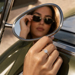 Lab grown diamond halo engagement ring in 14K white gold with side diamonds, resting against chrome car mirror.