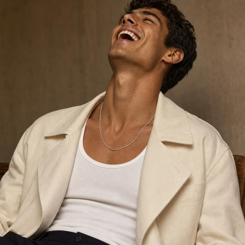 Close-up of a masculine model wearing a classic 2.1mm sterling silver box chain necklace against a taupe studio wall.
