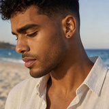 Close-up of a masculine black spinel stud earring in 925 sterling silver worn by a model against a beach backdrop.