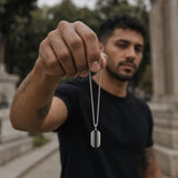 Close-up of a sterling silver dog tag pendant with black spinel stones held in a hand, showcasing the box chain.