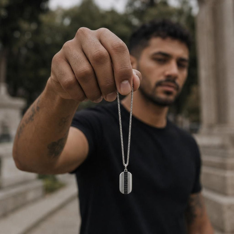 Close-up of a sterling silver dog tag pendant with black spinel stones held in a hand, showcasing the box chain.