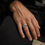 Close-up of a sterling silver wave ring featuring a row of round-cut black spinels on a male model hand.