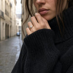 Black knit sleeve revealing a prominent statement ring from the Nyra 14K yellow gold collection on a European street scene.