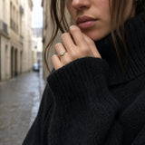 Black knit sleeve revealing a prominent statement ring from the Nyra 14K yellow gold collection on a European street scene.