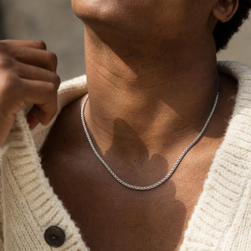 Close-up of a 925 sterling silver spiga wheat chain necklace worn around a man's neck with a cream knit cardigan.