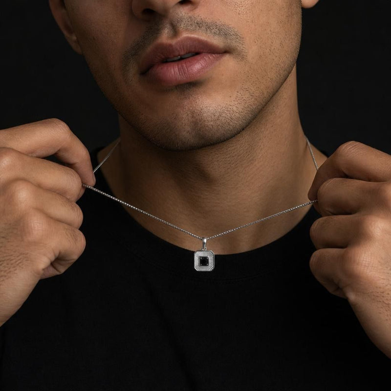Close-up of a masculine silver sunburst pendant with a center black spinel stone worn on a 24-inch polished box chain.