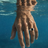 Asscher cut black spinel ring in 925 sterling silver worn on a hand submerged in clear blue water.